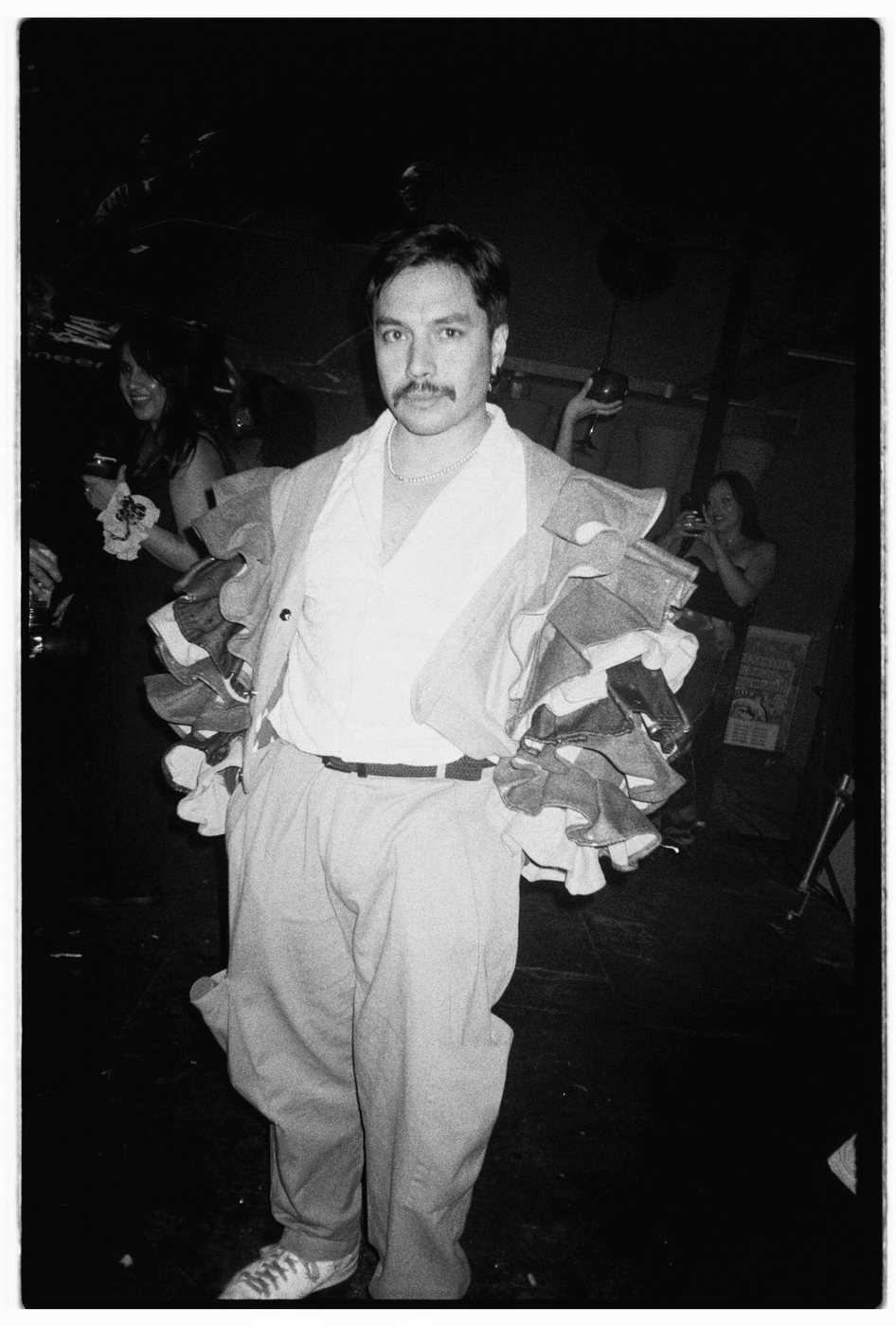 Mustached person standing in a ruffled jacket and wide trousers