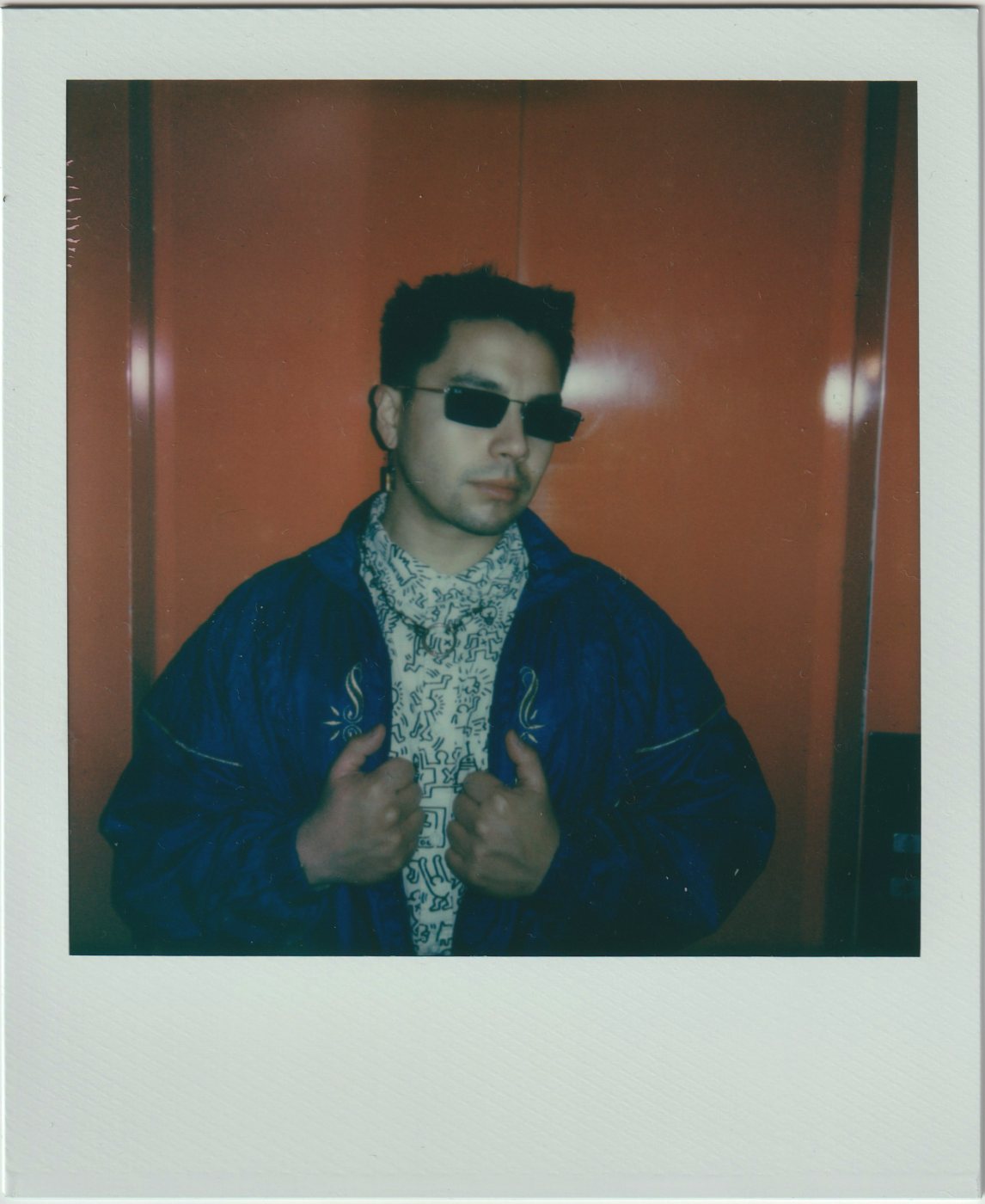 Person in a blue jacket and patterned shirt before an orange door
