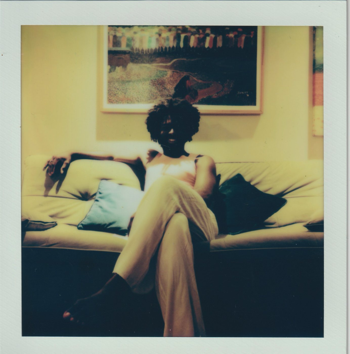 Person seated cross-legged on a cream sofa under a painting