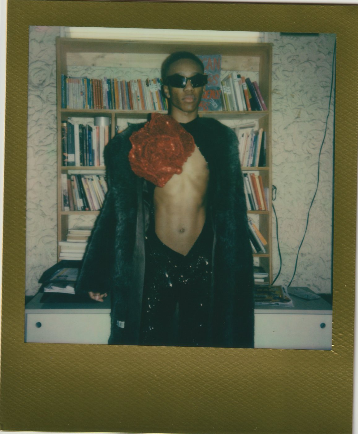 Person in sunglasses and a fur coat before a bookshelf